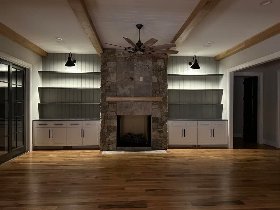 Living room with fireplace, built-in shelves, wood beams, ceiling fan, hardwood floors, and overhead lighting.