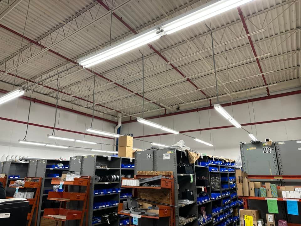 Warehouse interior with overhead lighting, shelving filled with parts, and a high ceiling.