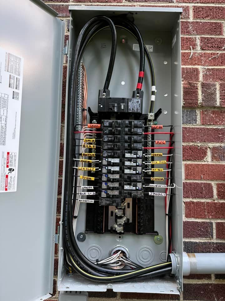 Open electrical panel with black wires, circuit breakers, and wiring against a brick wall.