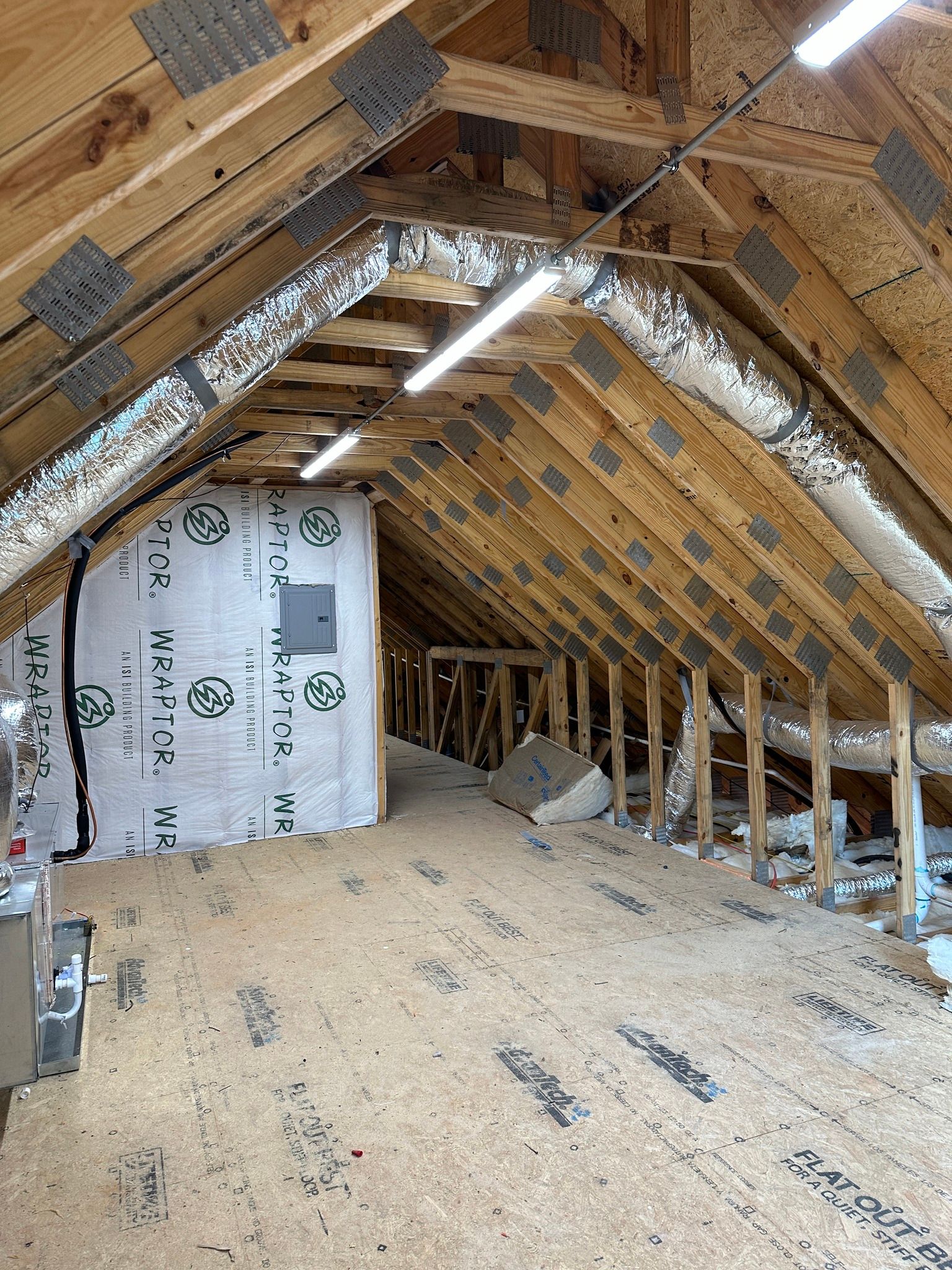Interior of an attic with wood framing, insulation, and a central electrical panel.