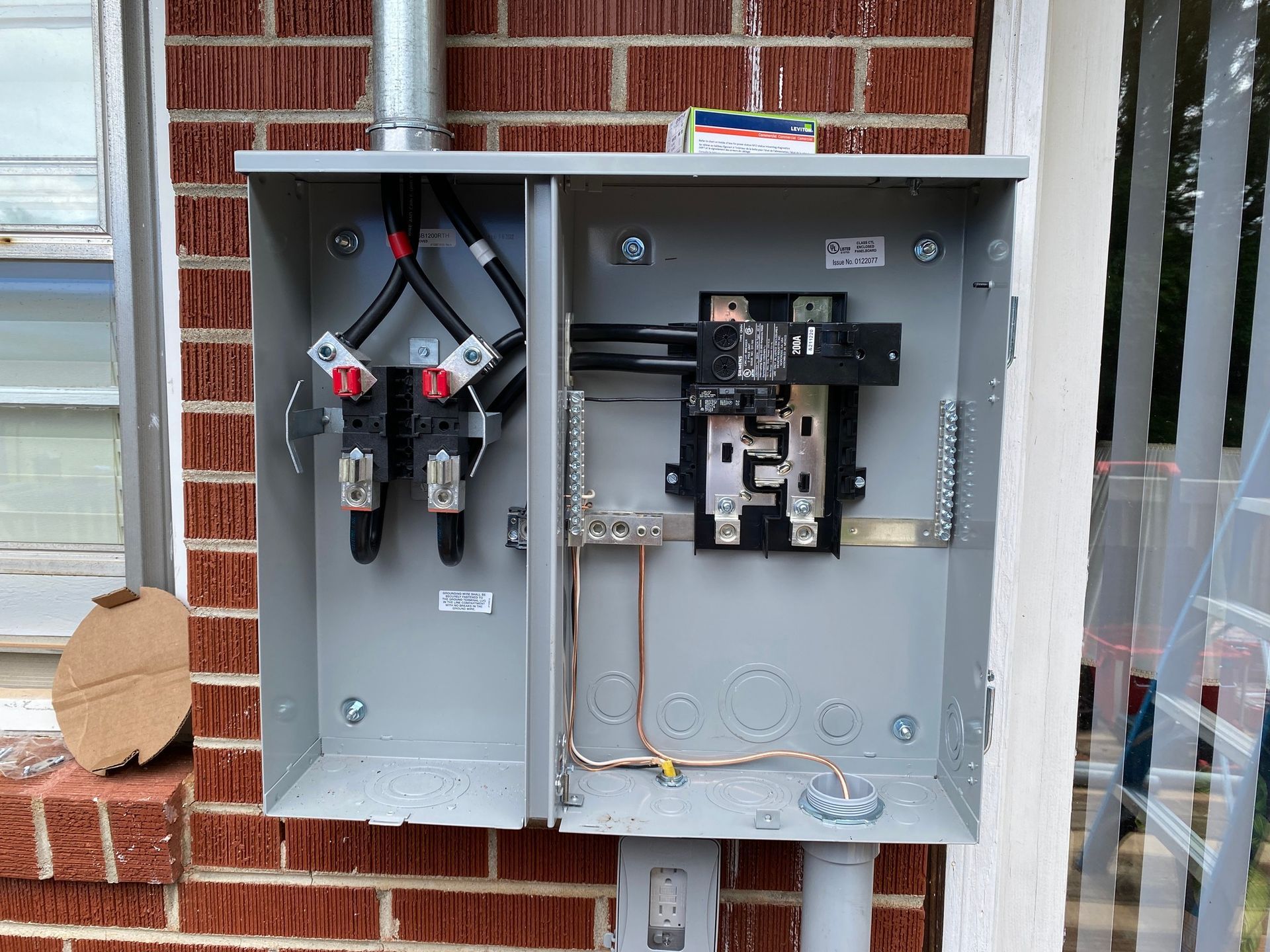 An open electrical meter box mounted on a brick wall, with exposed wires and breakers.