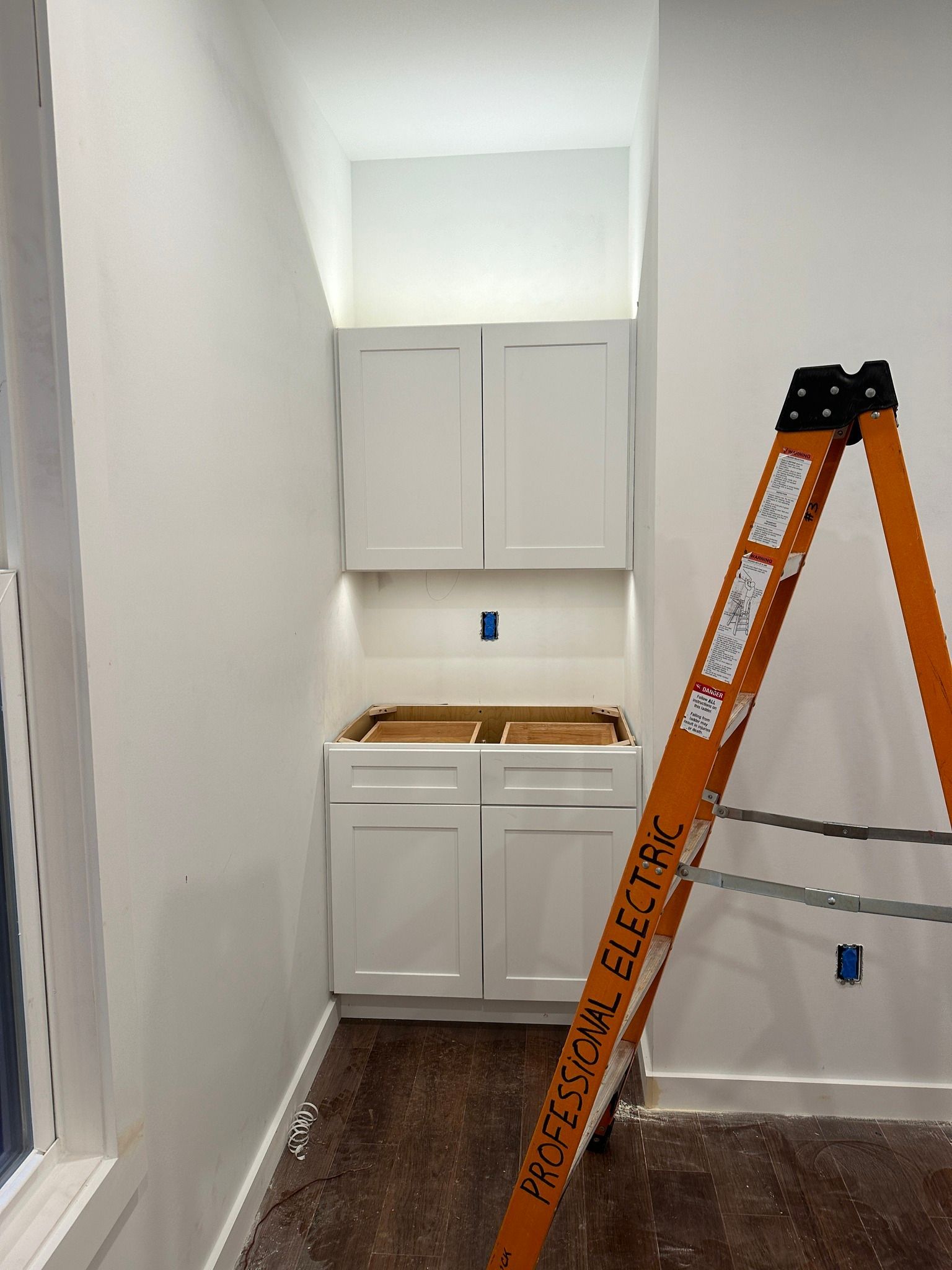 White kitchen cabinets installed in a wall niche. An orange ladder leans against the wall nearby.