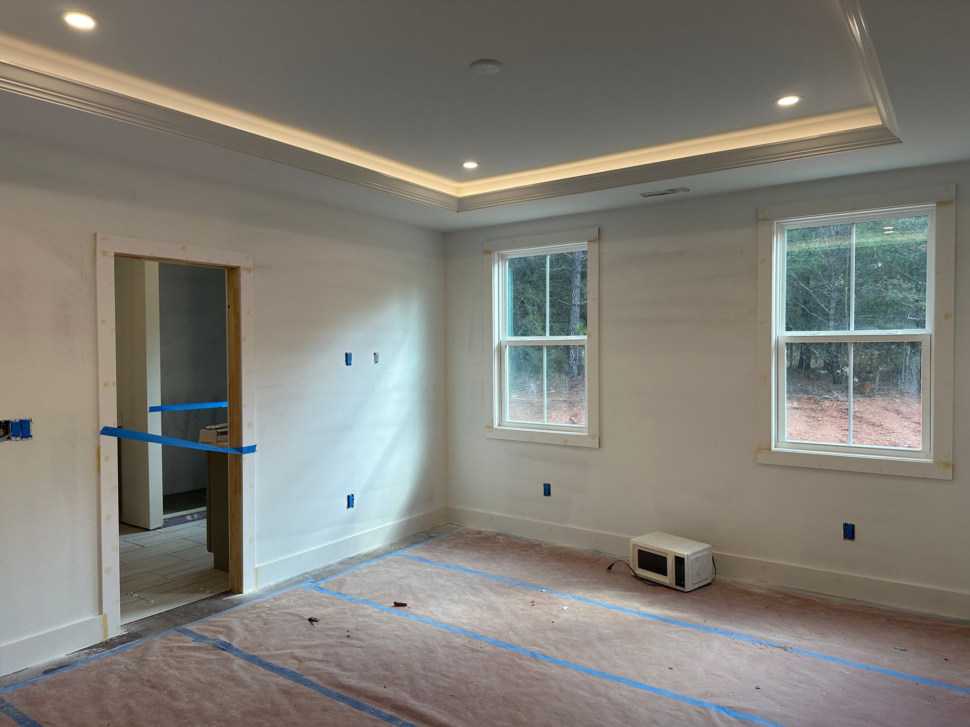 Empty room under construction with white walls, two windows, doorway, and decorative ceiling trim.