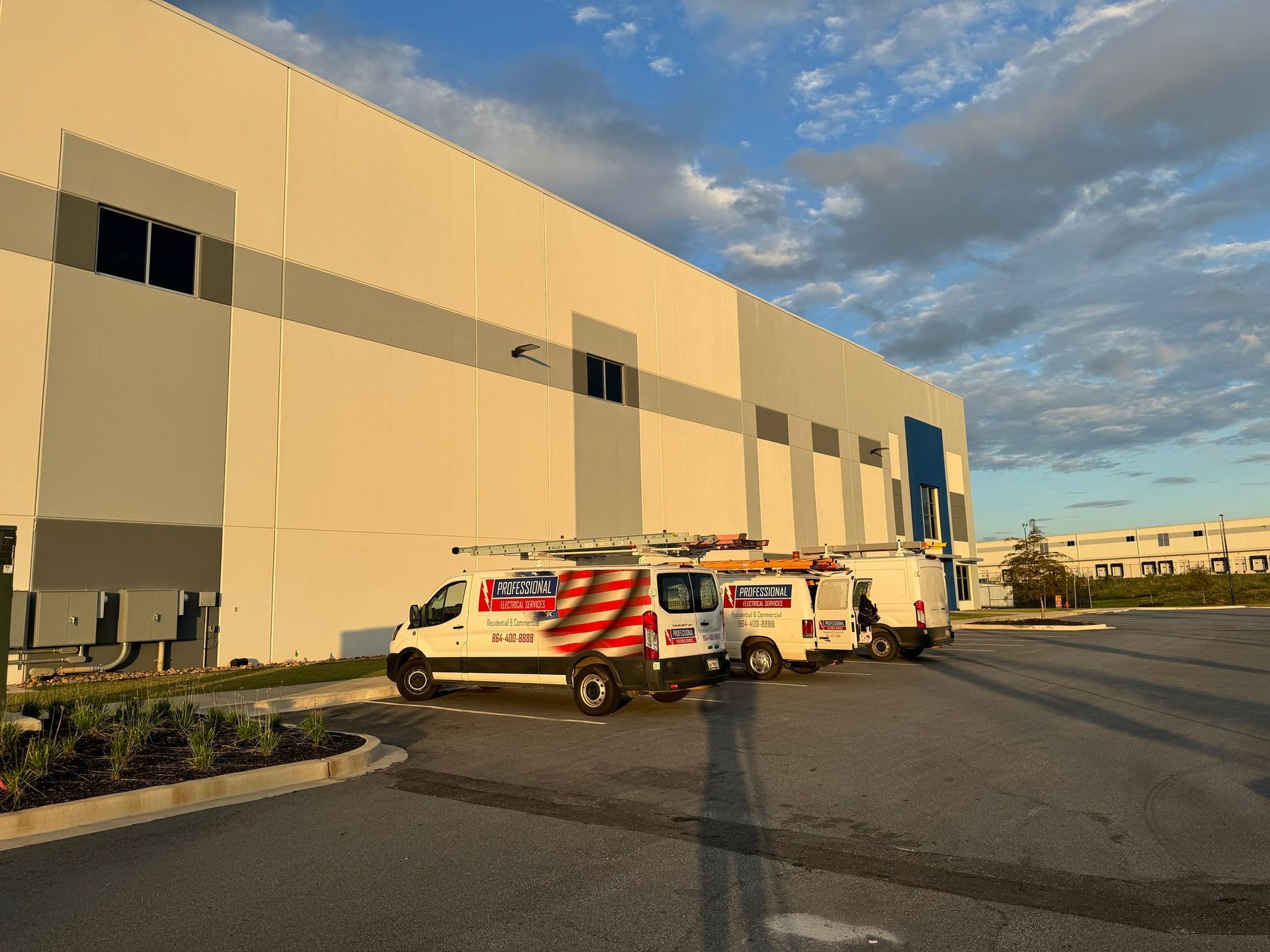 Three white service vans parked in front of a large industrial building. Cloudy sky overhead.