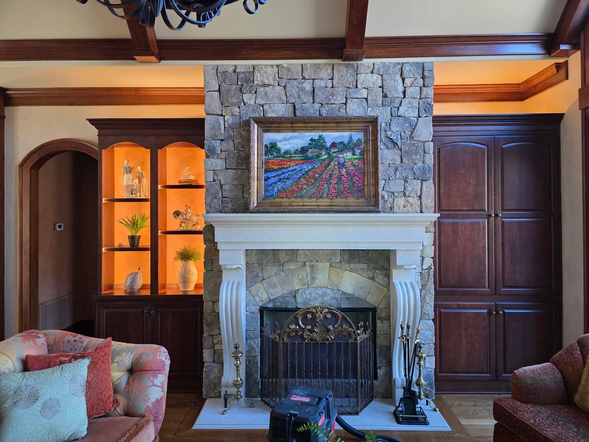 Fireplace with stone surround, artwork, and built-in cabinets in a living room with wooden beams and a sofa.