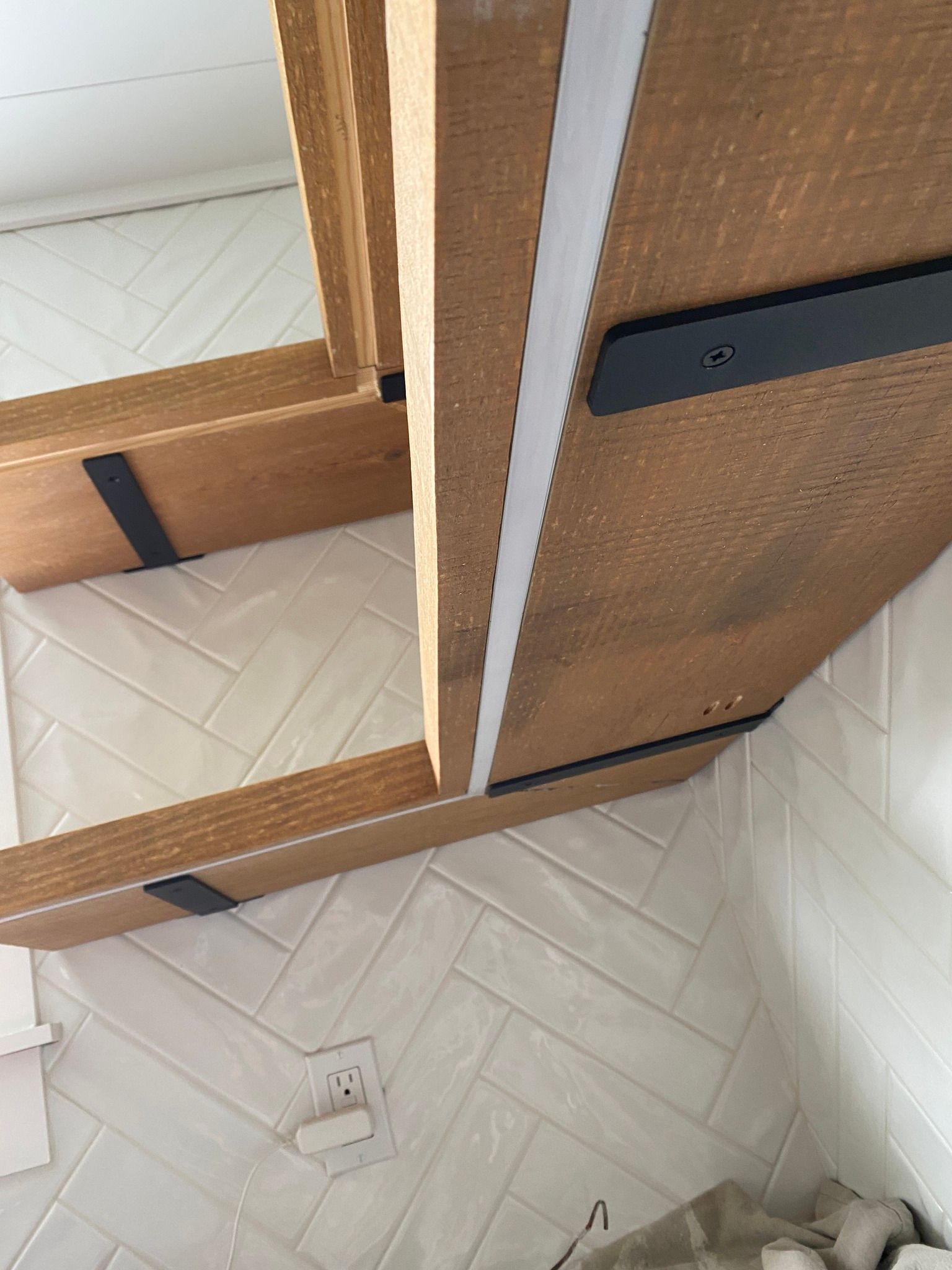 Wooden shelves supported by black brackets against a white tile wall.