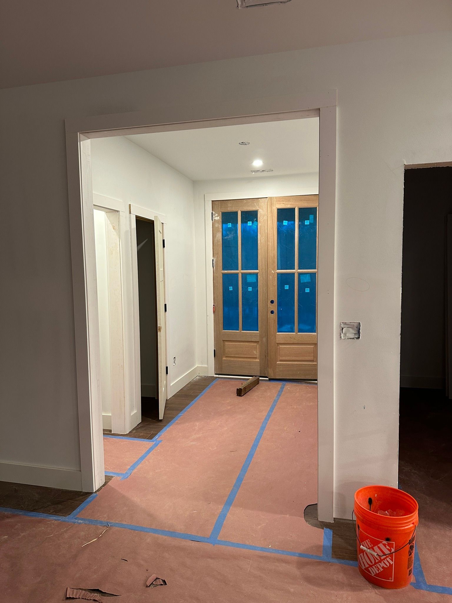 Interior hallway during construction; white walls, double doors, pink flooring, orange bucket.