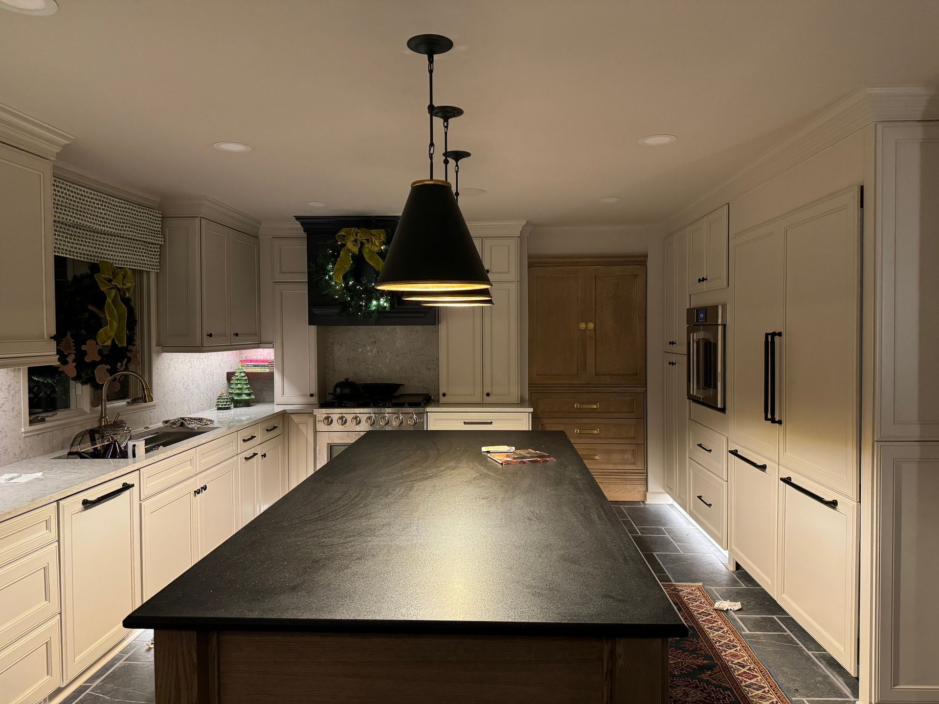 Kitchen with a dark island countertop and pendant lights. White cabinets, stove, and a rug.