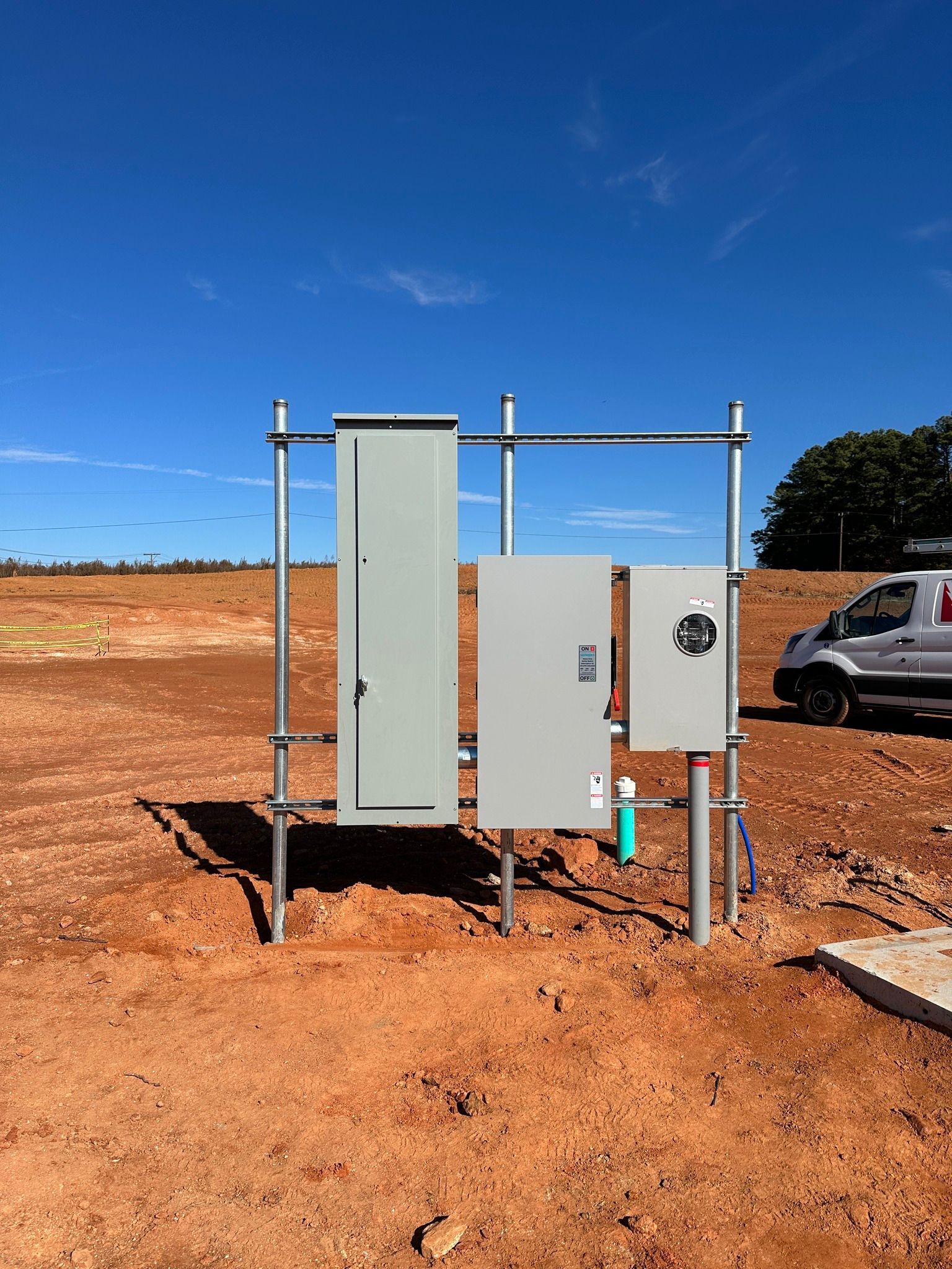 Electrical equipment on a construction site; gray metal boxes on scaffolding, sunny day.