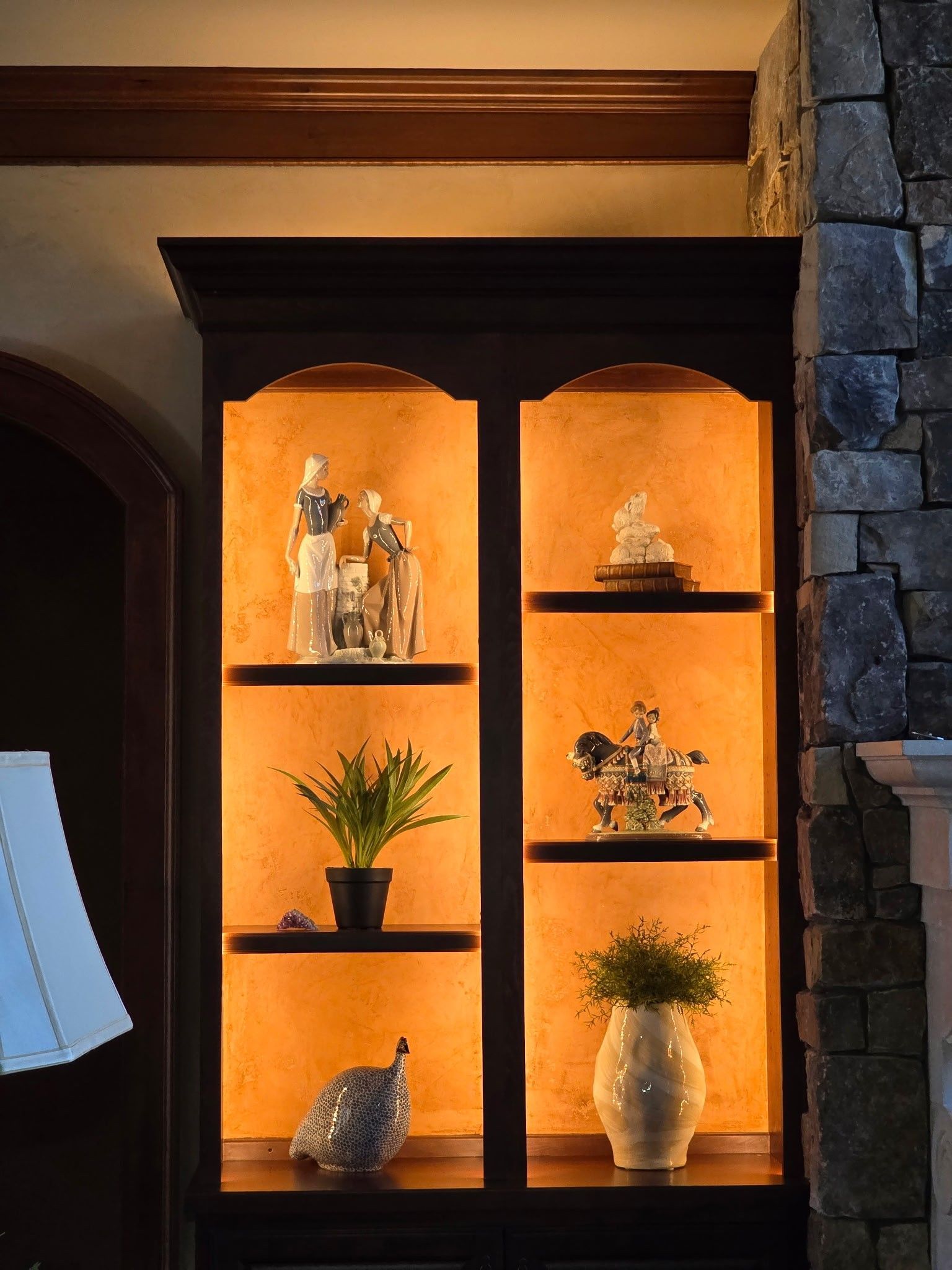 Black display cabinet with lit interior, holding figurines and plants.