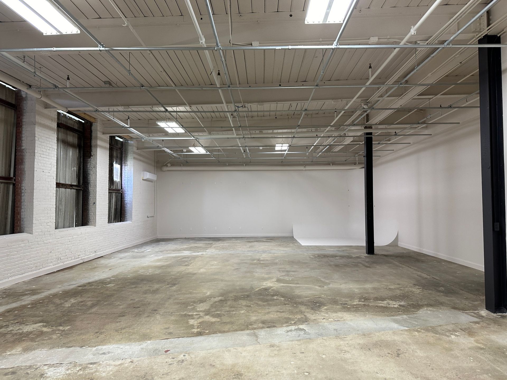 Empty, white-walled room with a concrete floor, two windows, and black support columns.