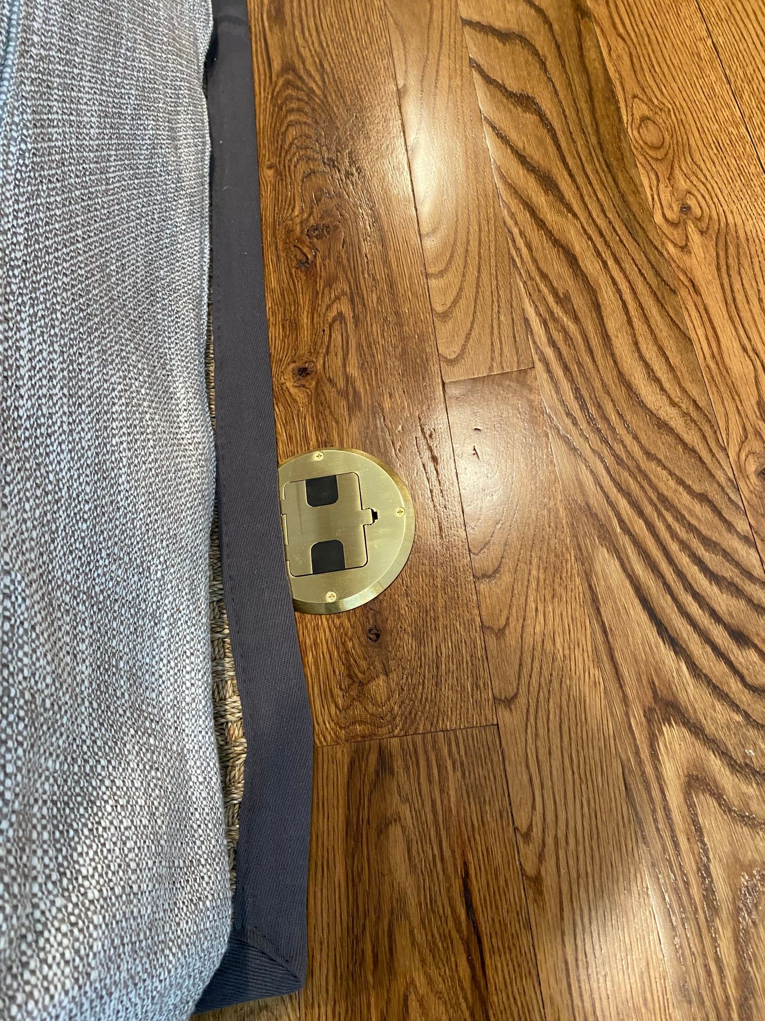 Light brown wooden floor with a yellow plastic electrical outlet cover. Beside is gray and dark blue fabric.