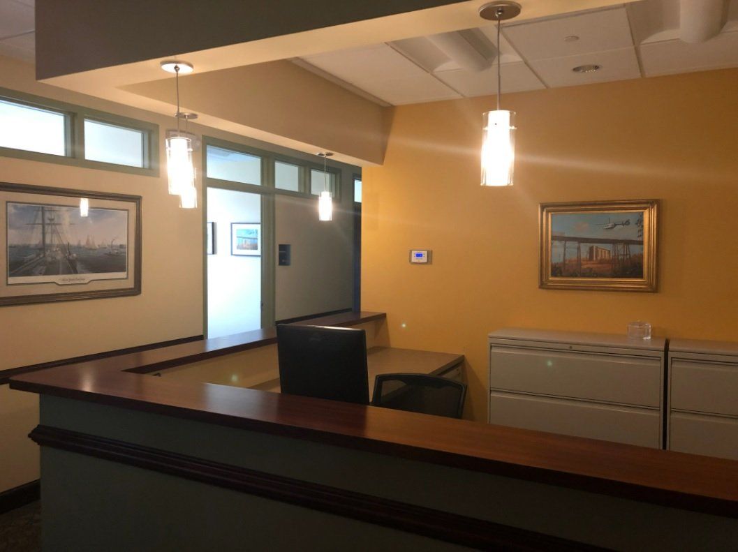 Reception area with wooden desk, yellow walls, artwork, and pendant lights.