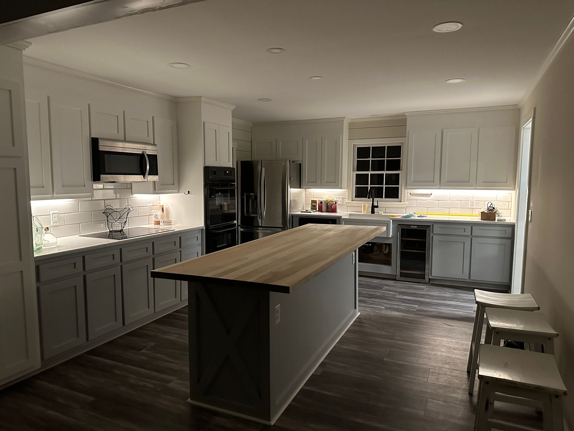 Modern kitchen with gray and white cabinets, wooden island, and warm lighting.