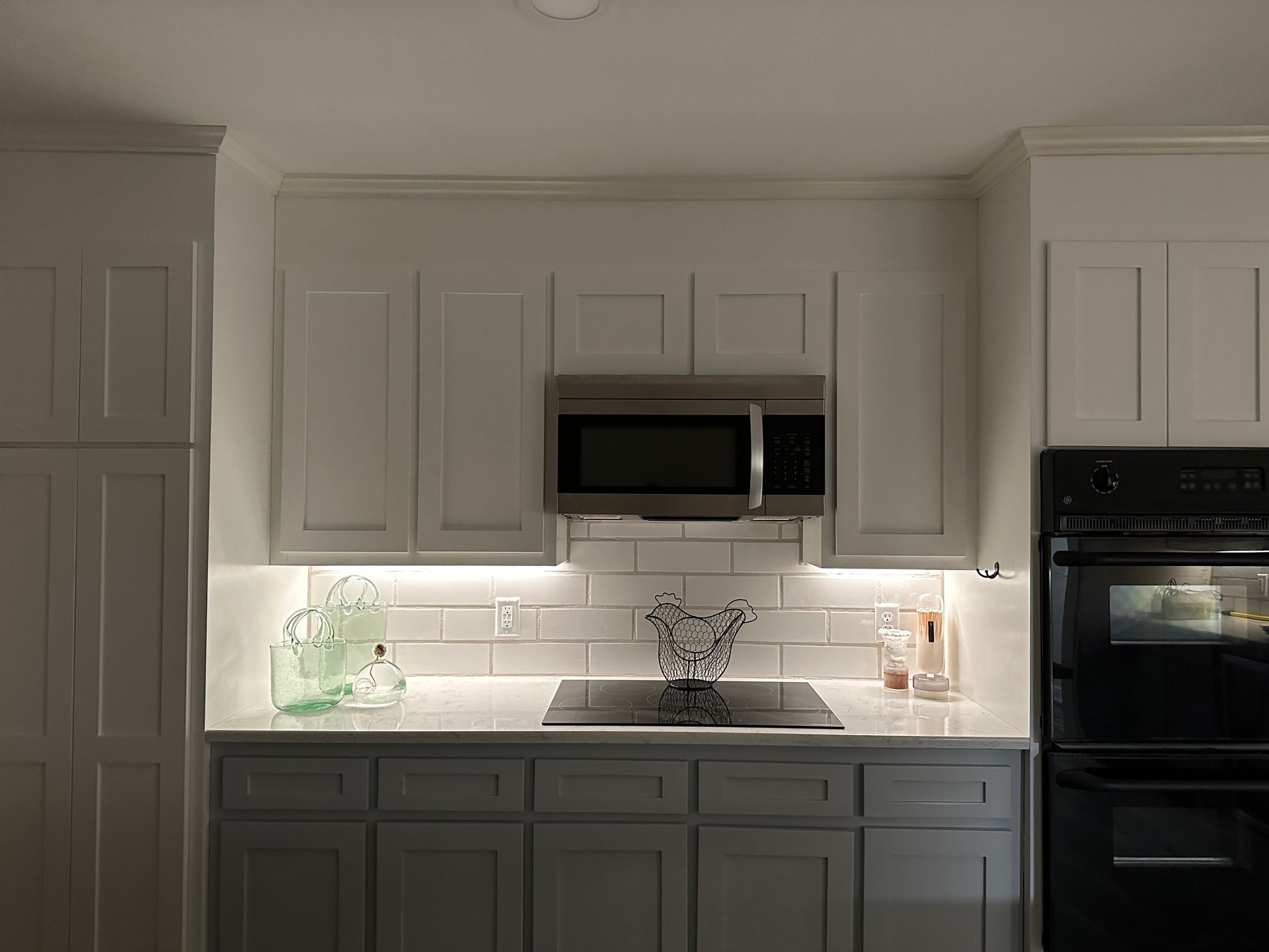 Kitchen with white upper cabinets, gray lower cabinets, microwave, and stove.