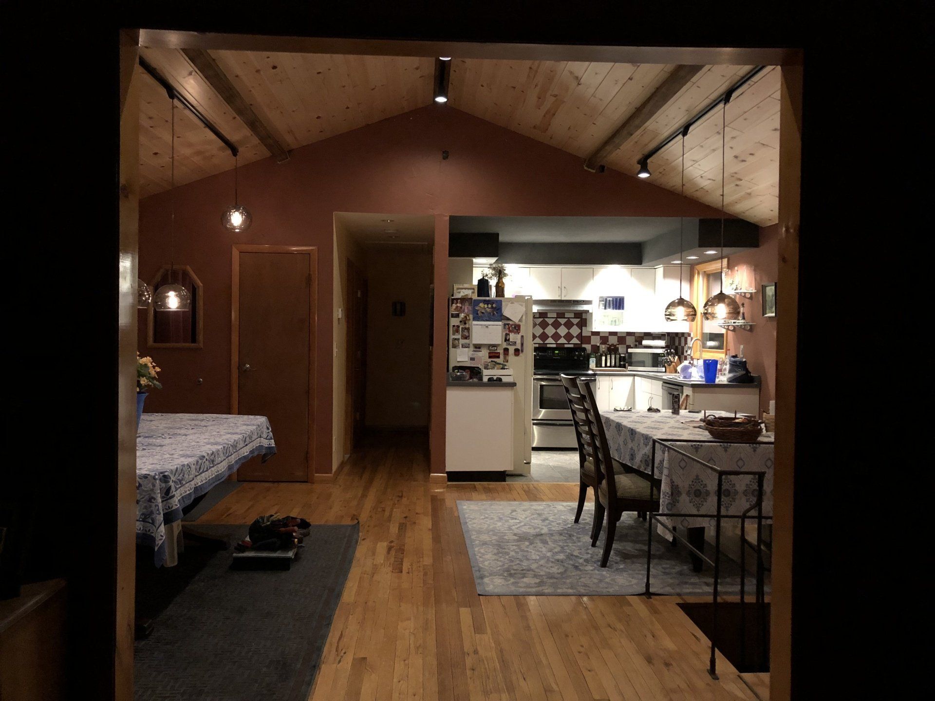 Interior view of a home with a wooden ceiling, hardwood floors, and a kitchen visible at the back.