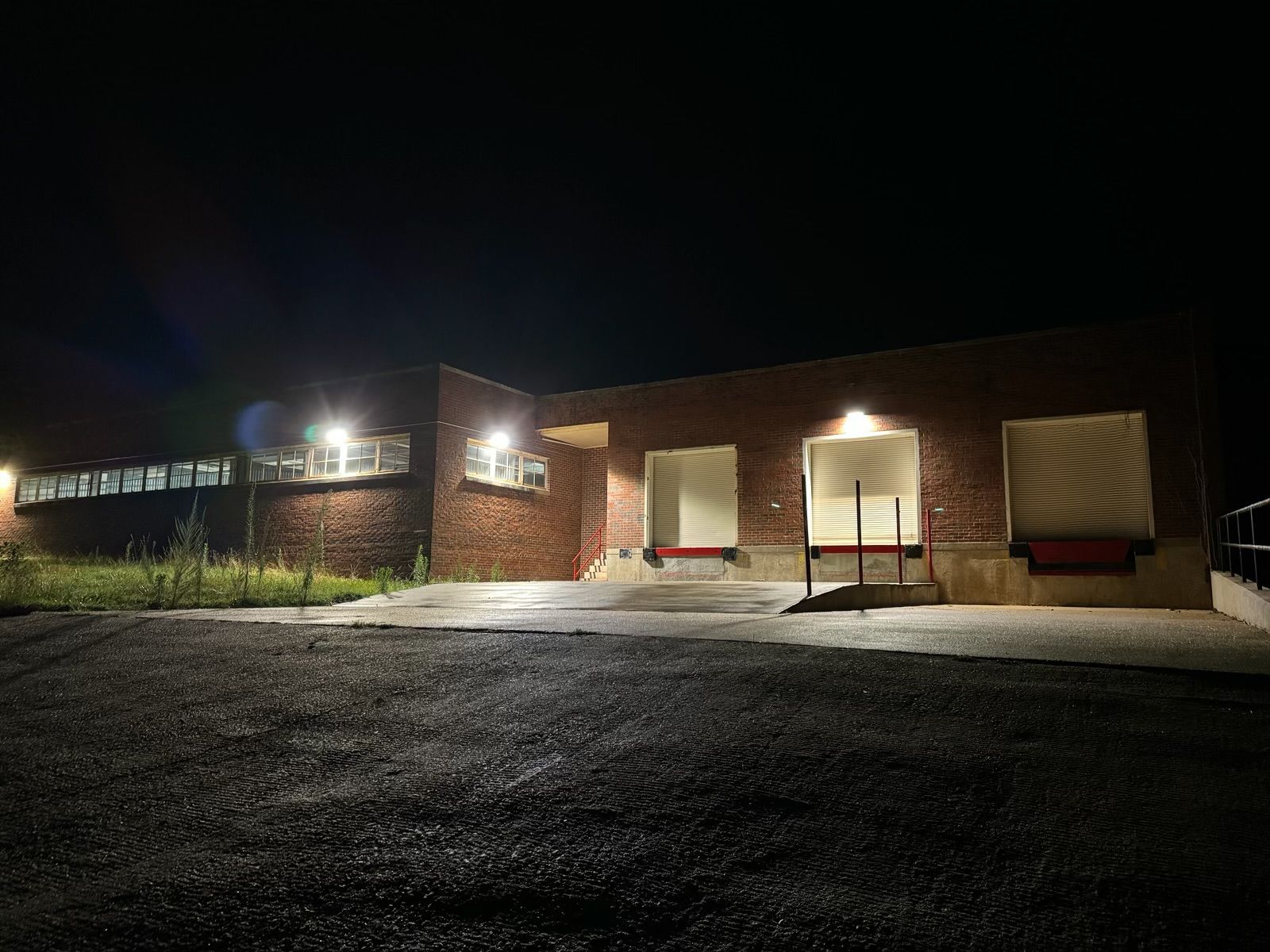 Brick building at night, lit loading docks. Gravel lot in foreground.