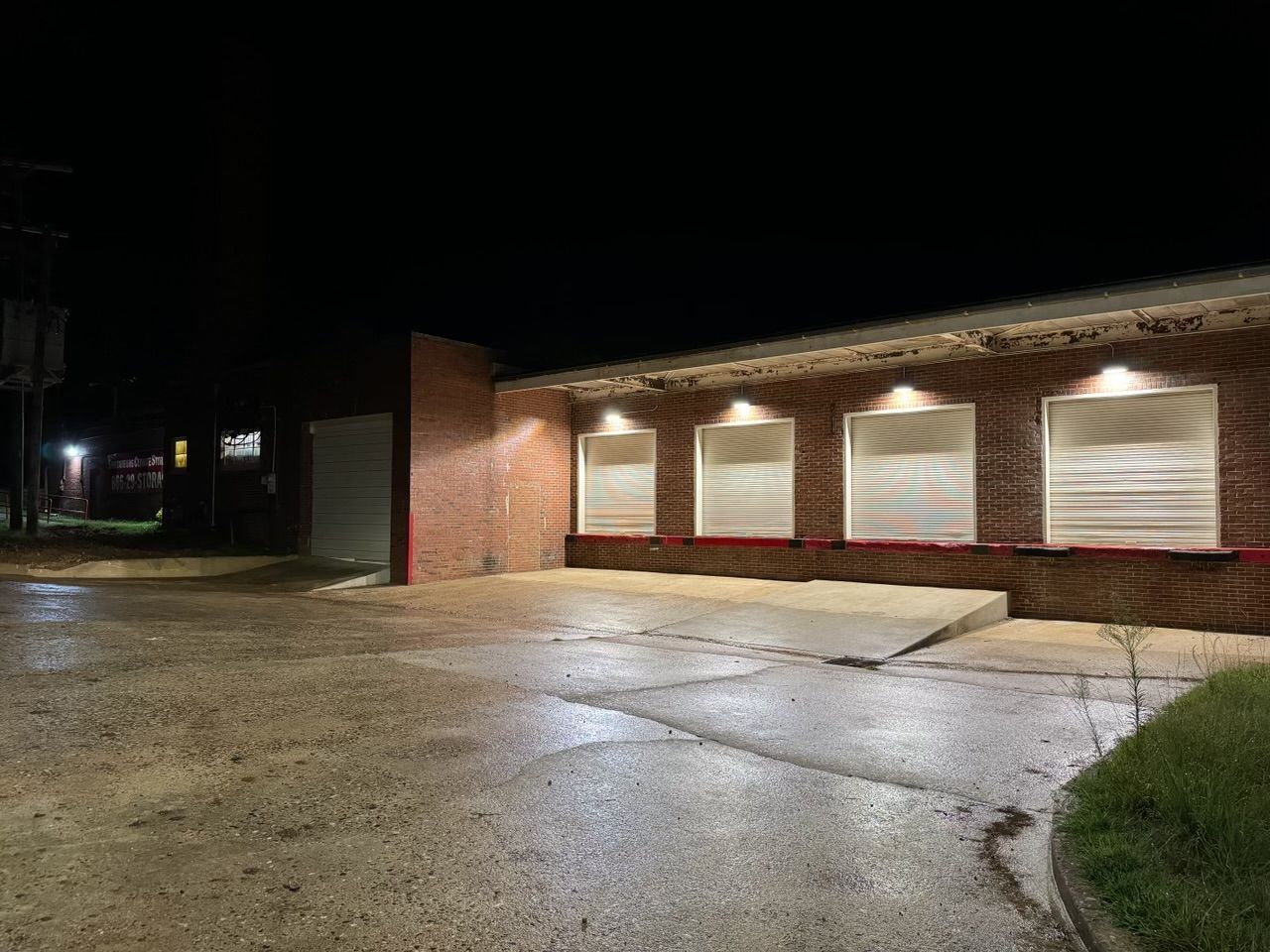 Night scene of a brick building with four closed loading dock doors. The ground is wet.
