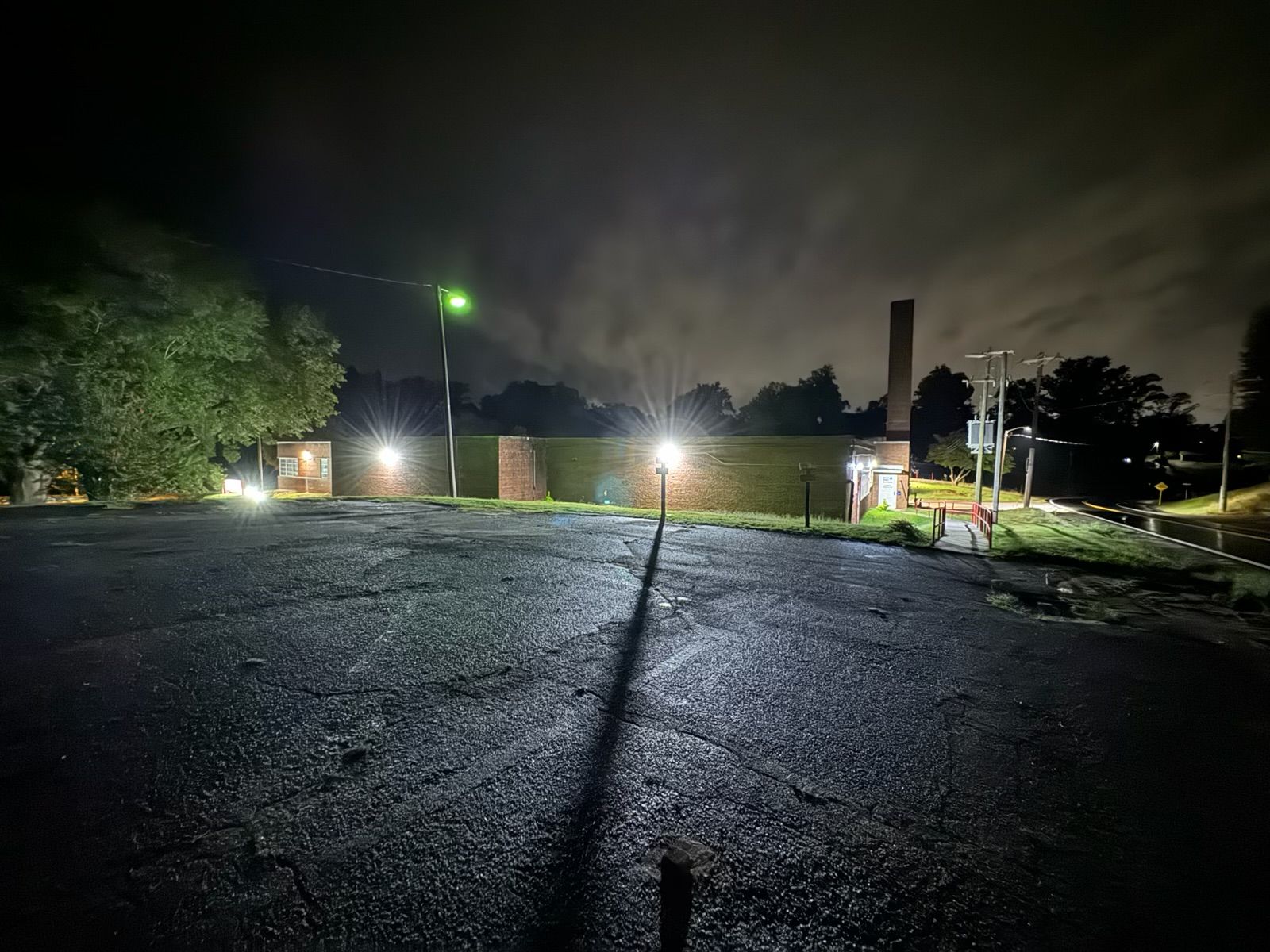 Dark, wet parking lot at night with several lit lamps casting shadows.