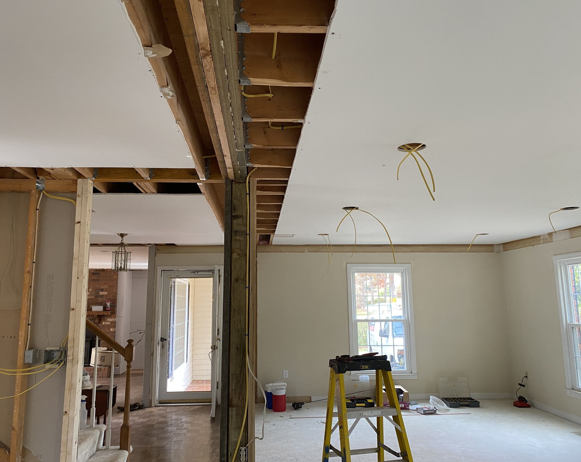 Interior room under renovation, exposed framing, drywall partially installed. Yellow ladder, wiring visible.