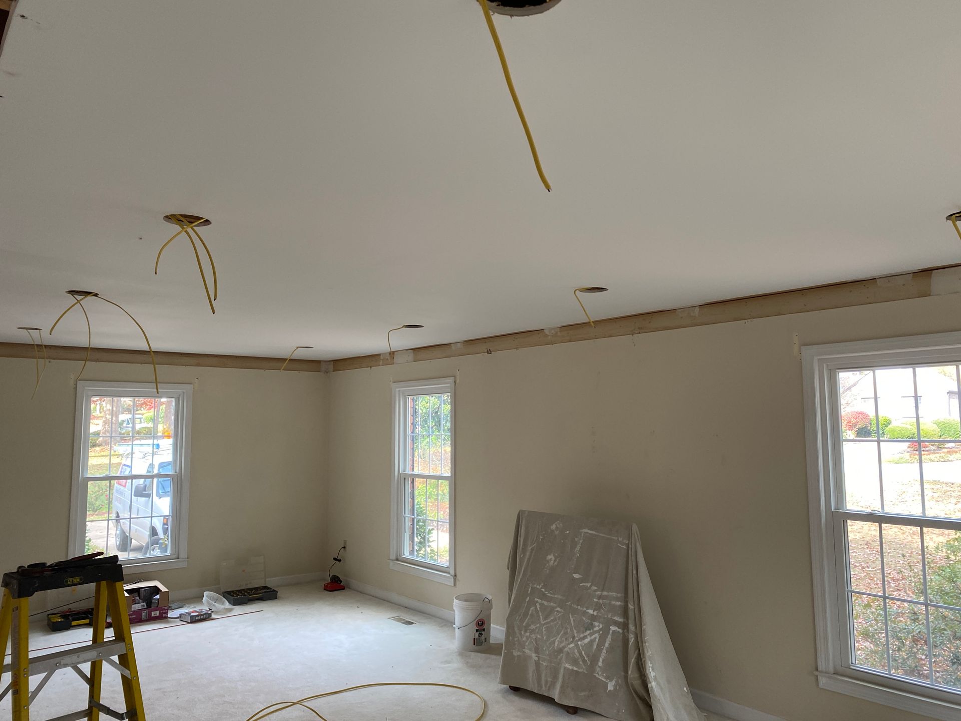 Interior view of a room under renovation. Ceiling with exposed wiring, walls with windows, and a ladder.