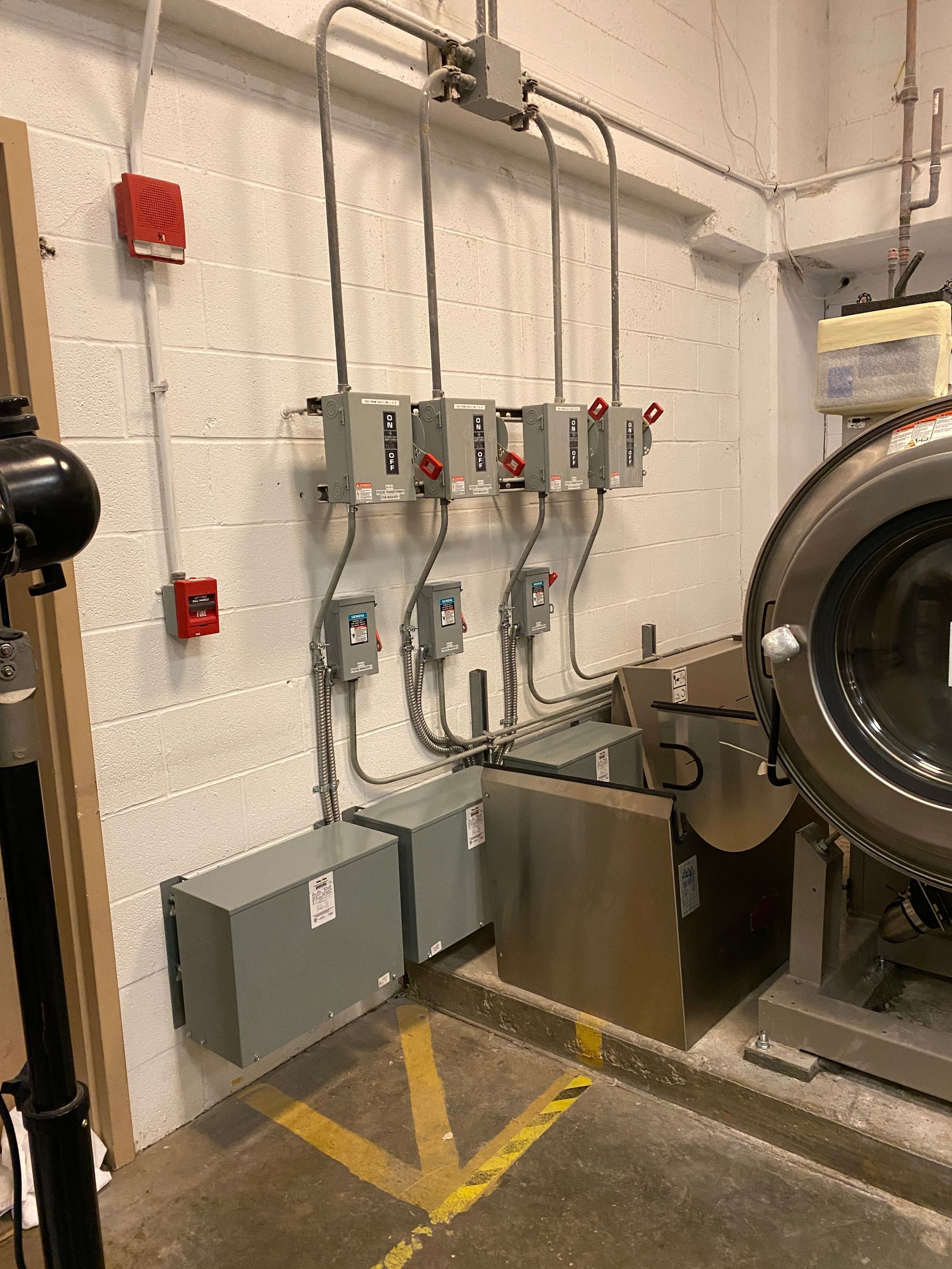 Electrical panel equipment mounted on a concrete wall in an industrial setting, next to a large machine.