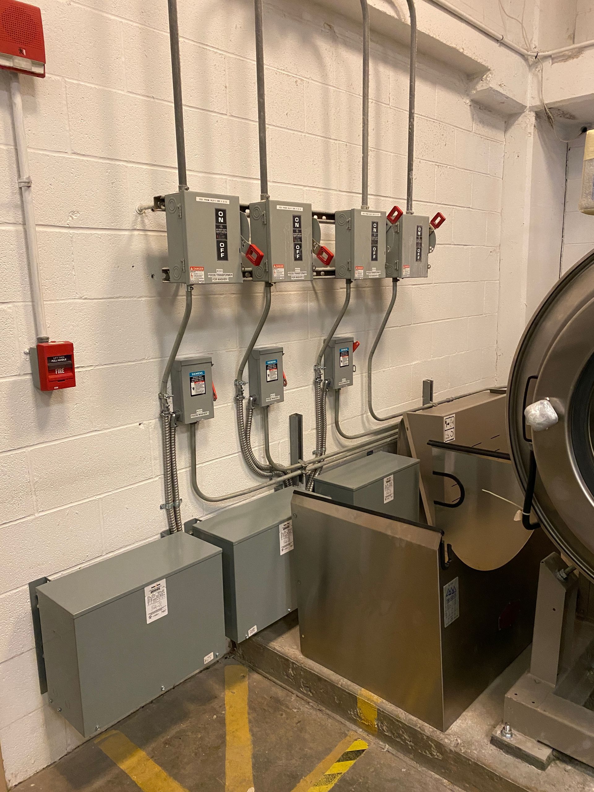 Electrical boxes and conduits mounted on a brick wall, with lower transformers and equipment.