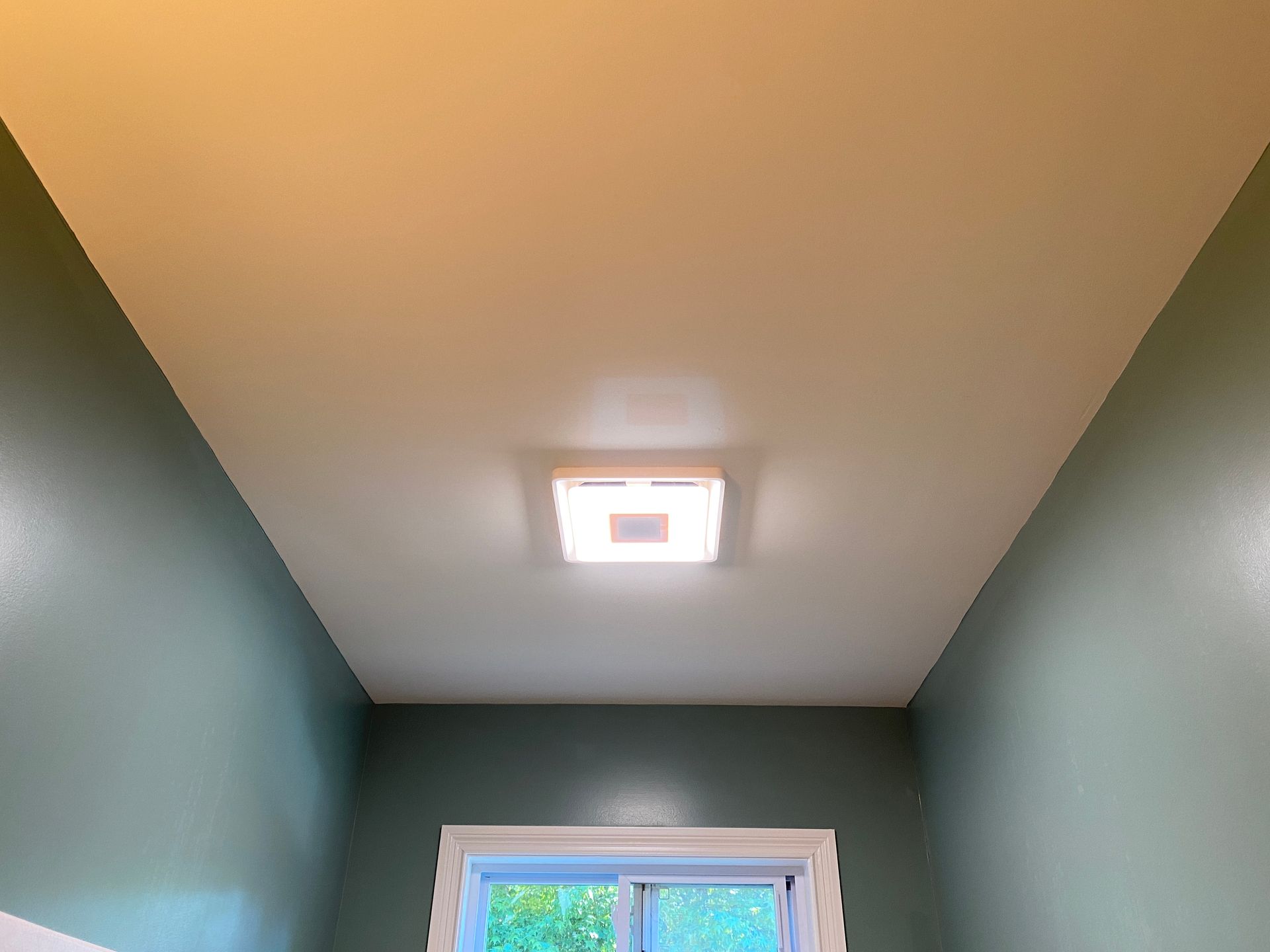 Green-walled bathroom with white ceiling and square ceiling light. A small window is at the bottom.