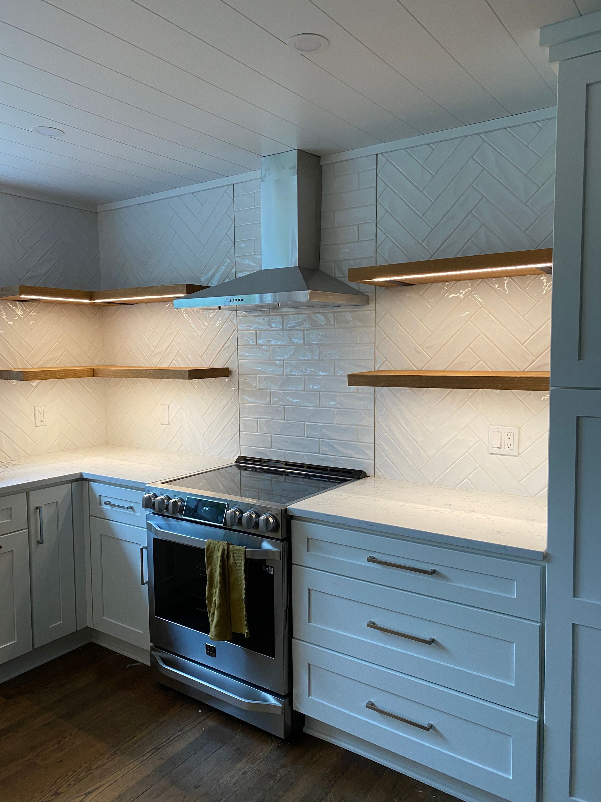 Kitchen with white cabinets, tile backsplash, stainless steel appliances, and wooden shelves.