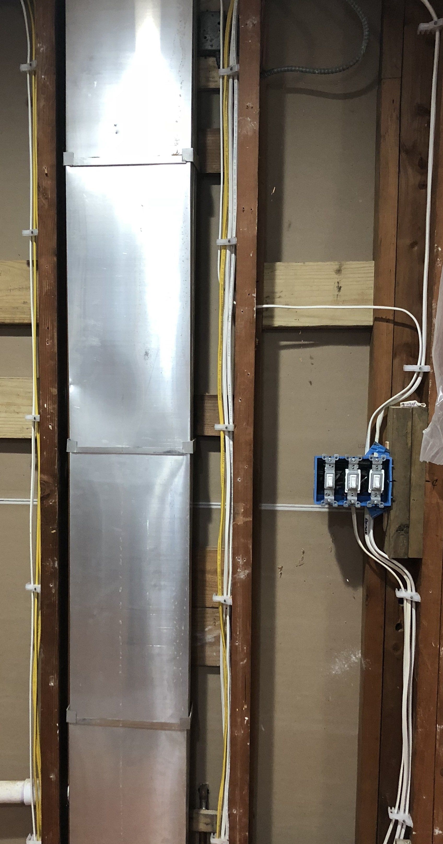 Exposed wall with metal ductwork, electrical box with wires, and wood framing.