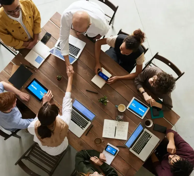 An overhead view of a diverse group having a meeting at a wooden conference table, with two people shaking hands.