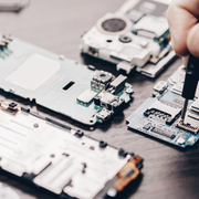 A hand uses a screwdriver to repair a mobile phone circuit board among various disassembled electronic components.