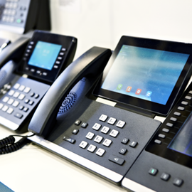 A silver smartphone rests on top of a tablet, which is placed over the keyboard of an open black laptop on a desk.