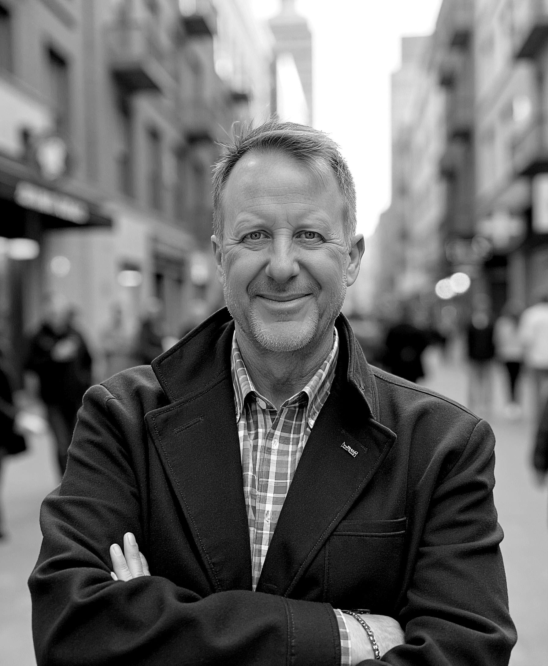 A man with a beard is smiling in front of a white brick wall.