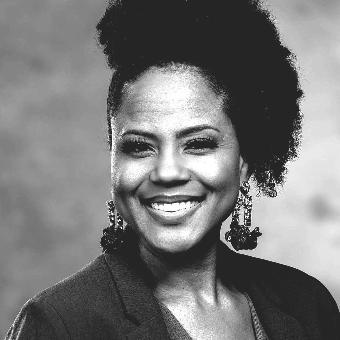 A woman with curly hair and earrings is smiling in a black and white photo.