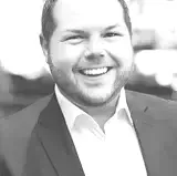 A man in a suit and white shirt is smiling in a black and white photo.