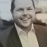 A man in a suit and white shirt is smiling in a black and white photo.