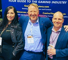 Three people posing for a picture in front of a sign that says your guide to the gaming industry
