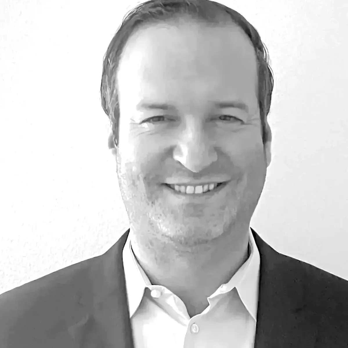 A man in a suit and white shirt is smiling in a black and white photo.