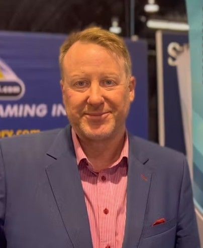 A man in a blue suit and pink striped shirt is smiling for the camera.
