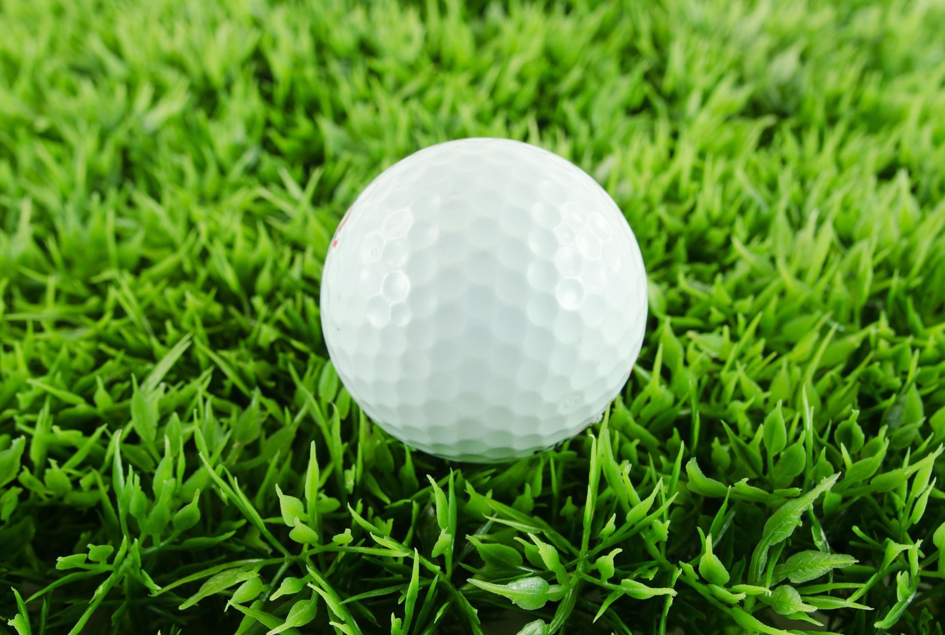 A golf ball is sitting on top of a lush green turf field.