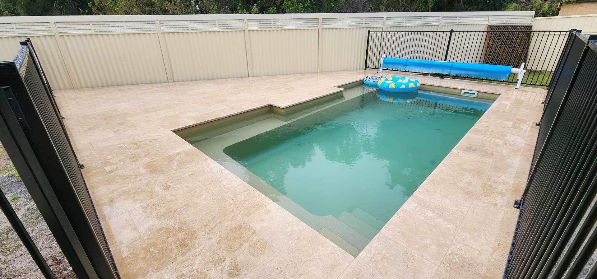 Small rectangular swimming pool surrounded by a beige concrete patio and black metal fence. A blue floaty is in the pool. — Clearwater Pools Hallidays Point In Hallidays Point, NSW