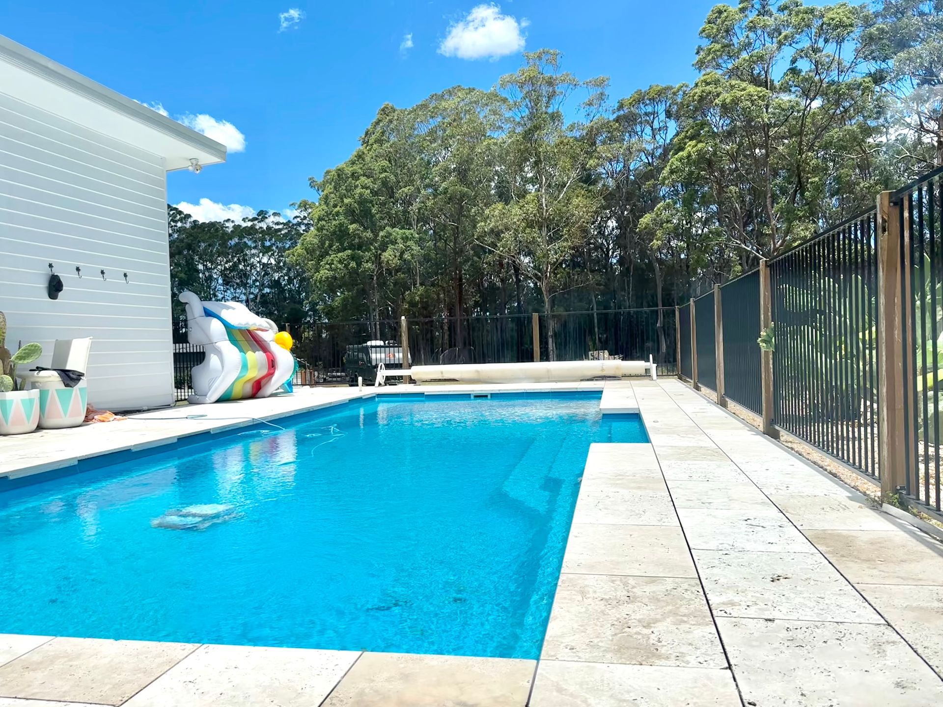 Rectangular swimming pool with grey tile surround and blue water. Wooden deck and dark fence in background.