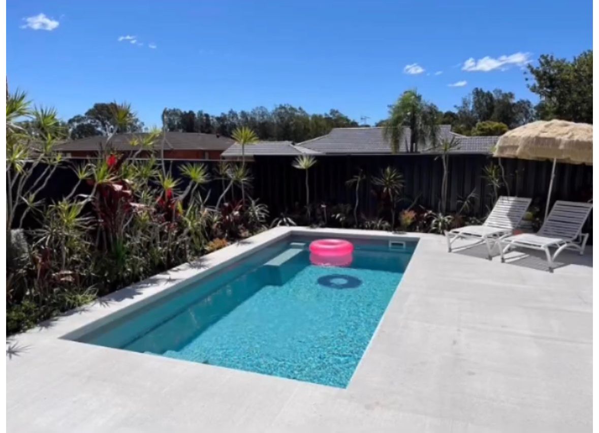 A rectangular swimming pool with blue water and pink inflatable ring, surrounded by a concrete patio and plants. — Clearwater Pools Hallidays Point In Hallidays Point, NSW