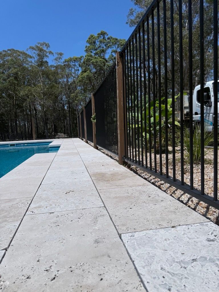 Rectangular swimming pool with grey tile surround and blue water. Wooden deck and dark fence in background.