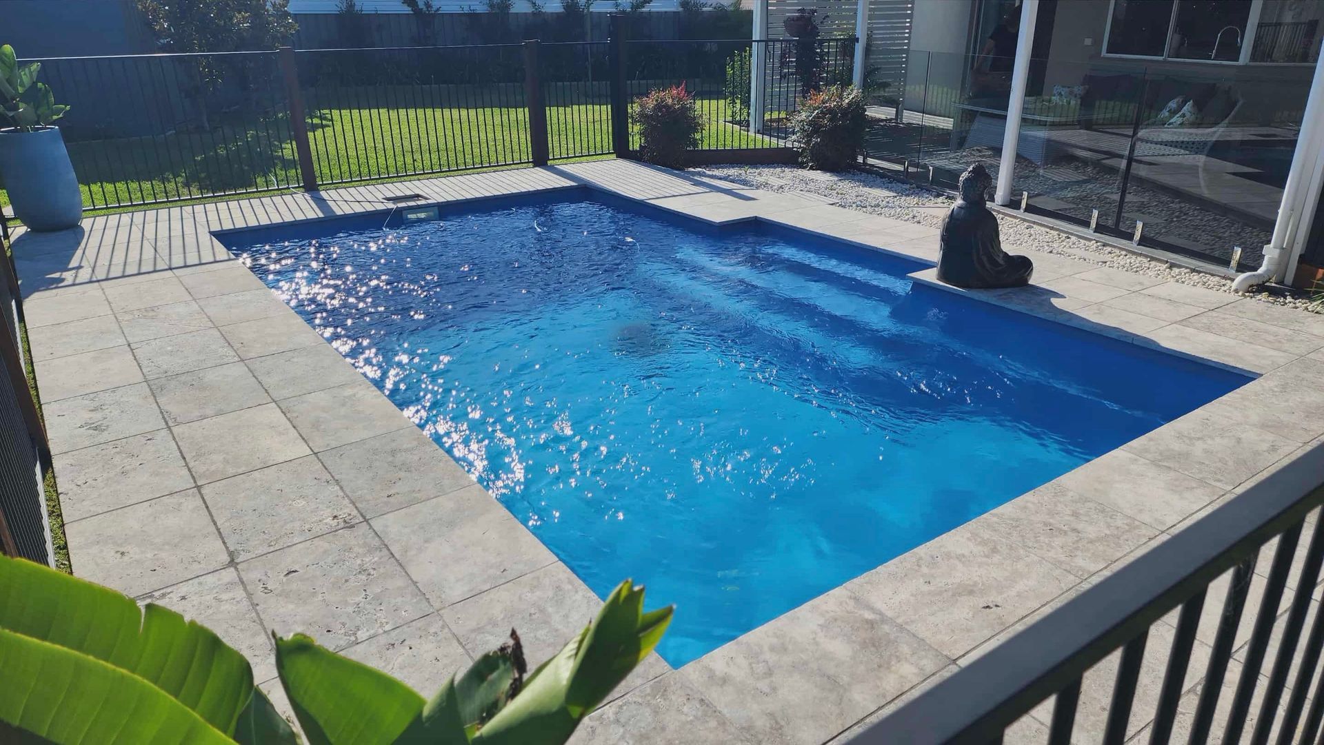 Small rectangular swimming pool with blue water surrounded by stone pavers, Buddha statue nearby.