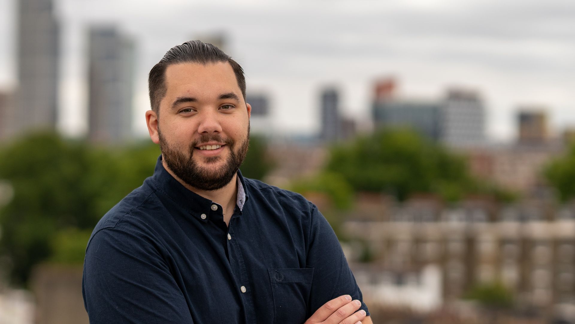 Ben Greenstreet of Birkby Bridge is standing with his arms crossed in front of a city skyline.