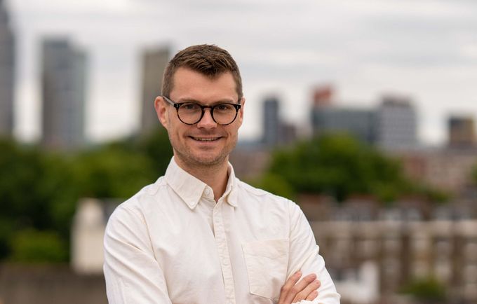 Rob Quirk, founder of Birkby Bridge wearing glasses and a white shirt in front of a city skyline.