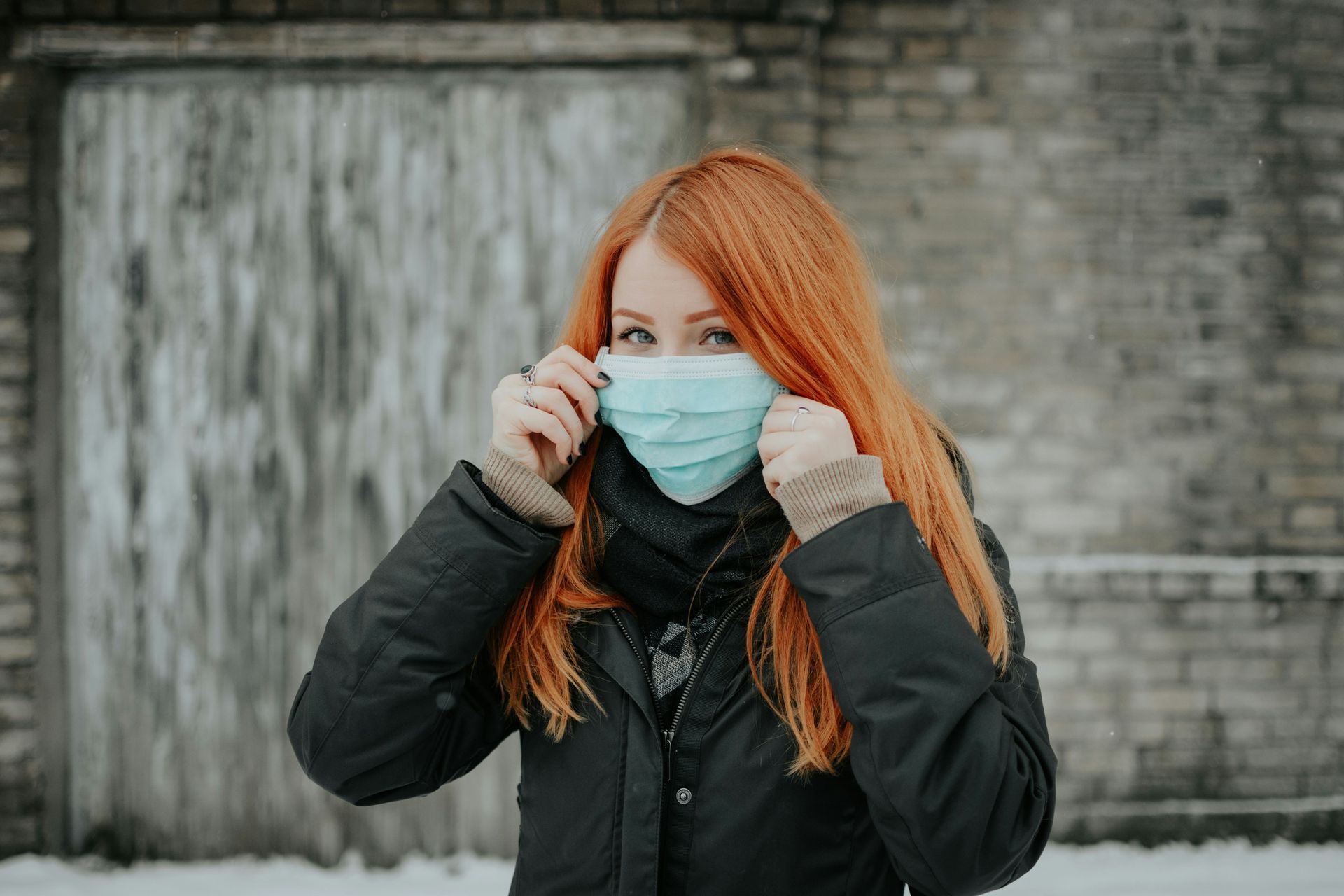 A woman with red hair is wearing a medical mask.