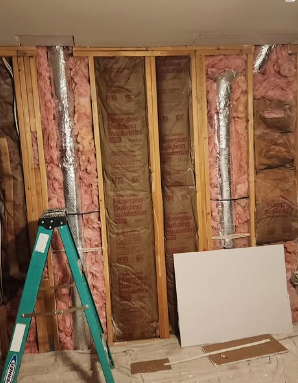 Interior wall under construction with pink insulation, ductwork, and ladder.